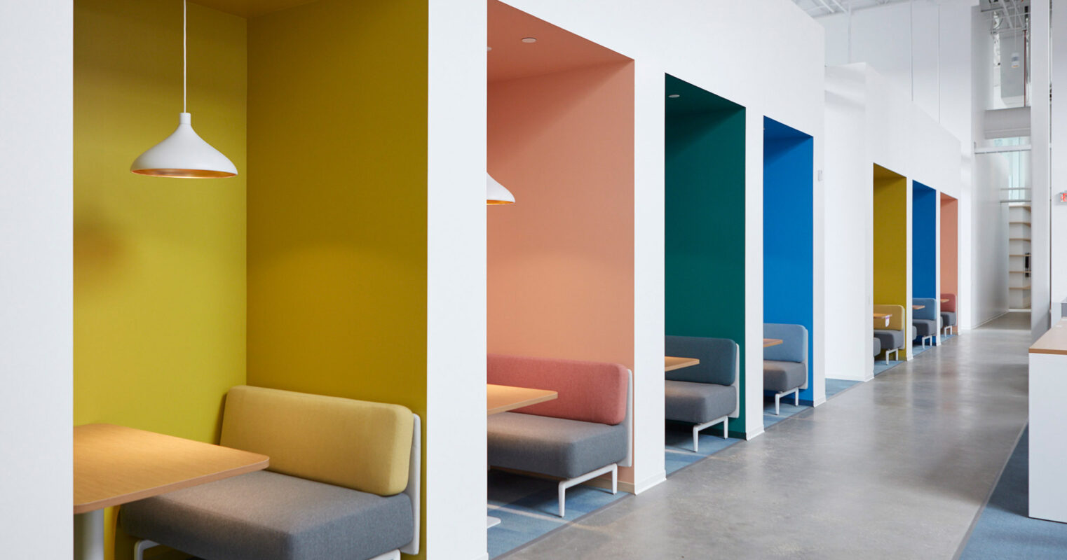 Minimalist waiting area with a vibrant color scheme, featuring a succession of recessed seating nooks in yellow, orange, teal, and blue, each accented with a sleek pendant light and simple bench seating.