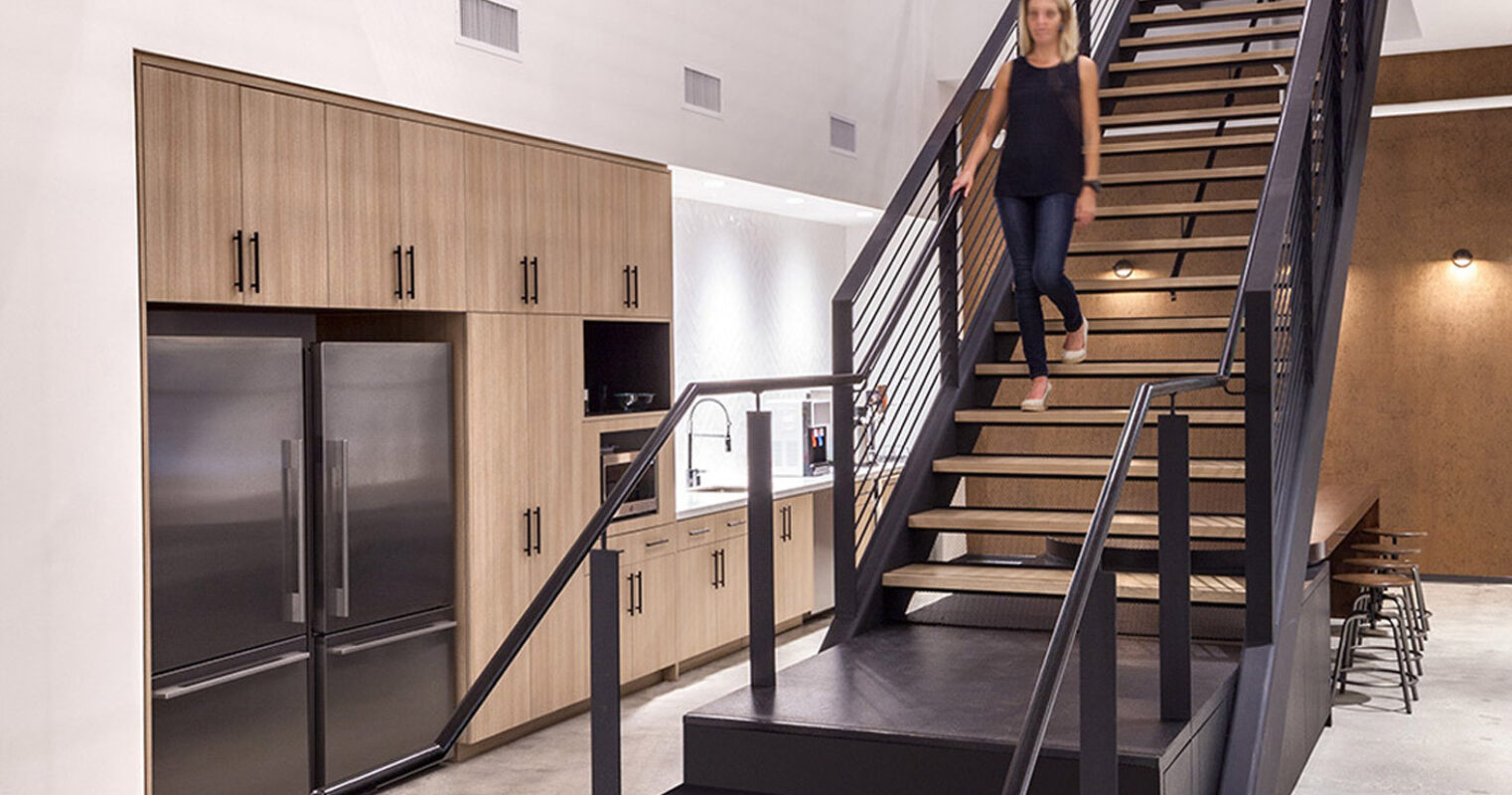 Minimalist staircase with contrasting black steps and white risers anchors the space, flanked by sleek wooden storage cabinets. Overhead, playful pendant lights dangle, enhancing the industrial loft feel of the high-ceiling interior.