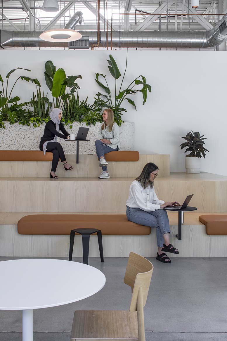 Indoor office space with individuals seated on benches, greenery in background.