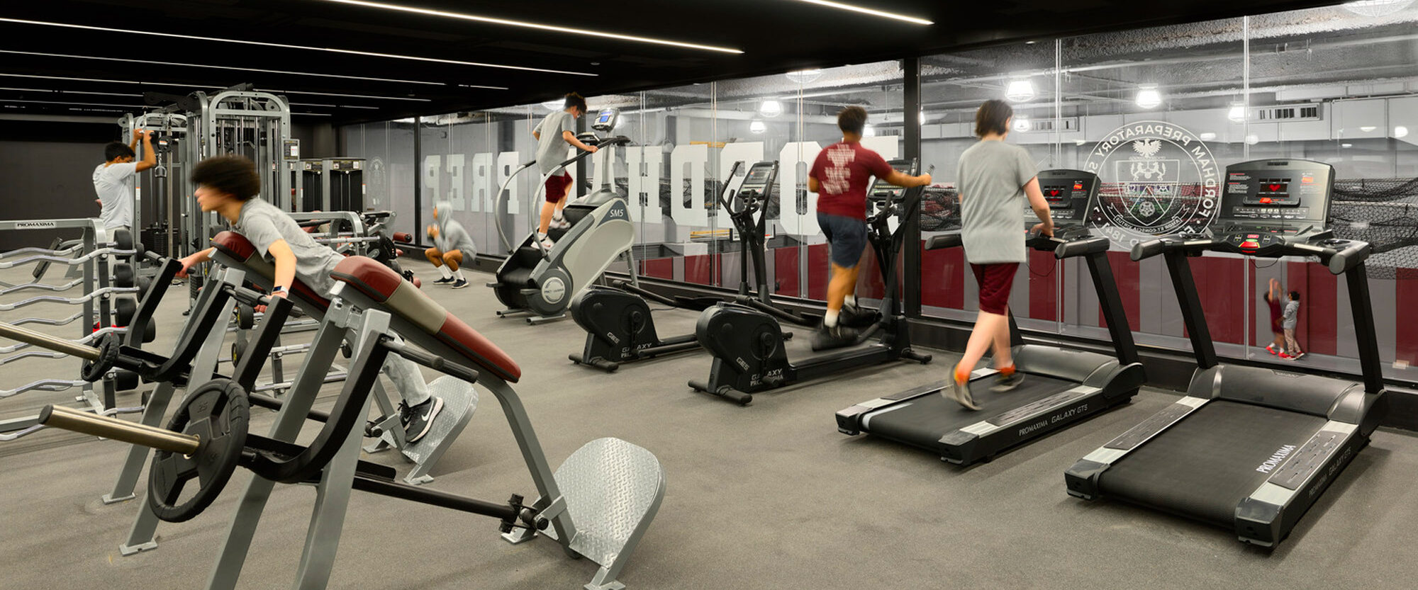 Modern gym interior featuring an array of fitness equipment, including treadmills, ellipticals, and weight machines, with mirrored walls enhancing the space's depth and motivational graphics adorning the walls for an energetic workout environment.