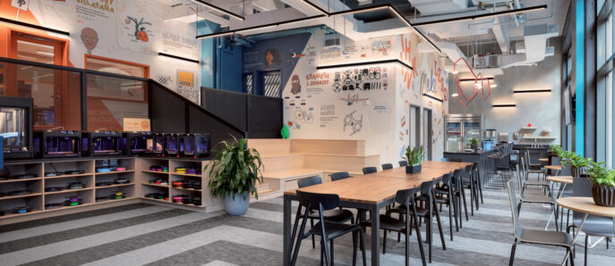 Modern open-plan office with vibrant graphics adorning the walls, featuring a communal wooden table, sleek metal chairs, and ample shelf space with colorful storage units; natural light enhances the room's urban loft aesthetic.
