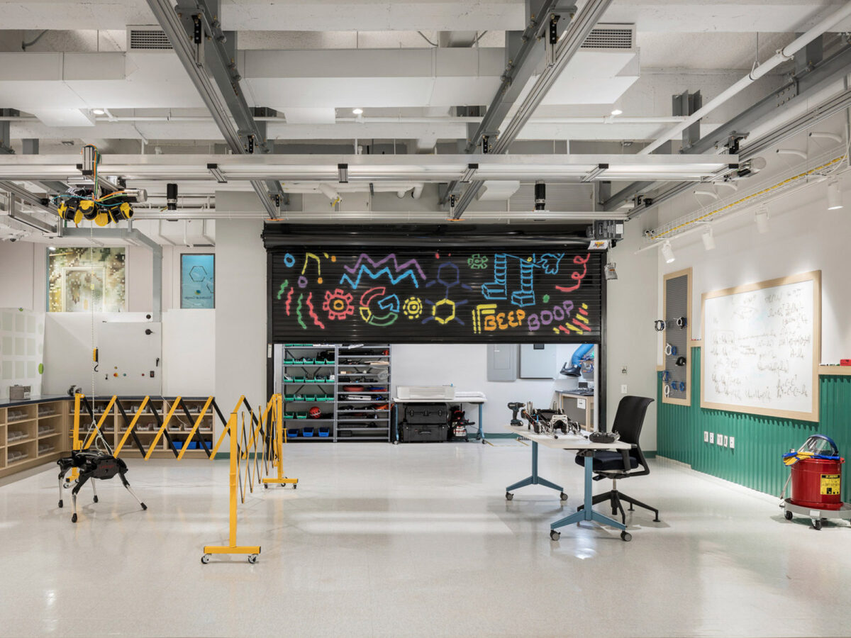 Modern industrial-style workspace featuring exposed ceiling utilities, polished concrete floors, and a large blackboard with vibrant chalk art. A collaborative environment is suggested by the mobile workstations and various tools for creative projects. The space exudes functionality blended with creative flair.